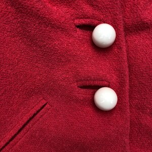 May include: Close-up of two white buttons on a red fabric surface. The buttons are round and have a smooth finish.