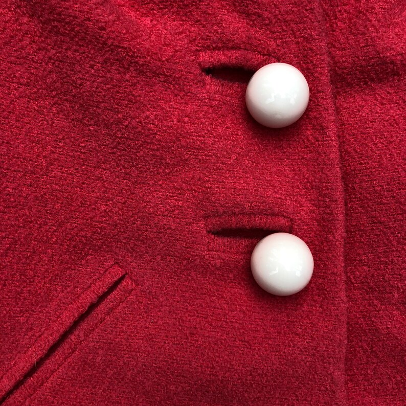 May include: Close-up of two white buttons on a red fabric surface. The buttons are round and have a smooth finish.