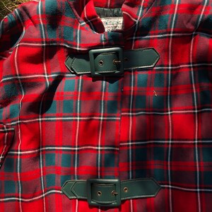 May include: Red and green plaid cape with two leather belts with buckles. The label reads "Country Place".