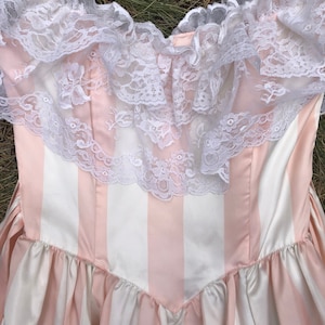 May include: A pink and white striped dress with a white lace trim around the neckline.