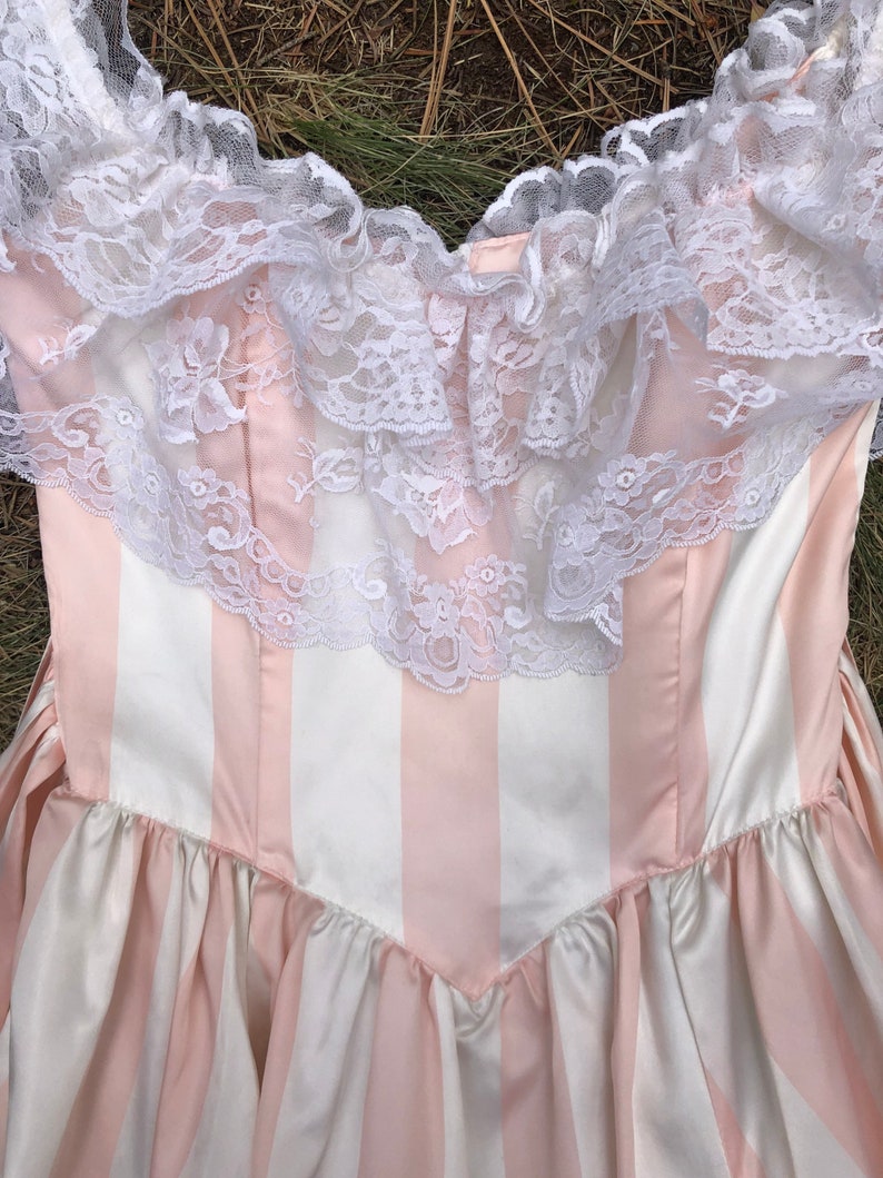 May include: A pink and white striped dress with a white lace trim around the neckline.