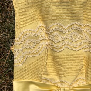 May include: A yellow sleeveless dress with a white lace bodice and a matching yellow satin bow at the waist.