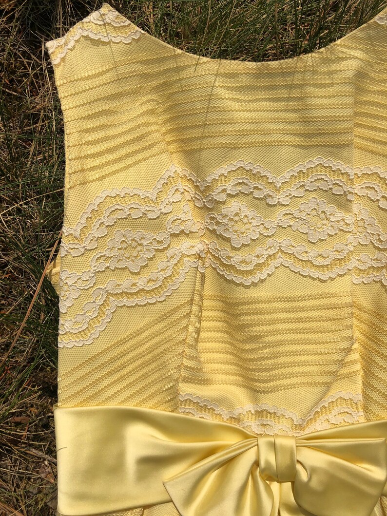 May include: A yellow sleeveless dress with a white lace bodice and a matching yellow satin bow at the waist.