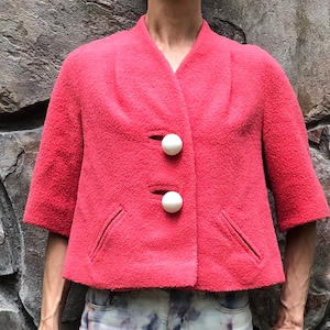 May include: A short-sleeved, pink, cropped jacket with a V-neck and two white buttons.