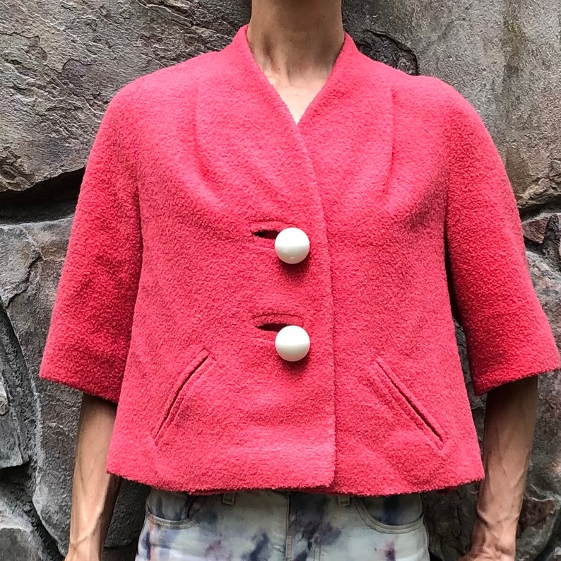 May include: A short-sleeved, pink, cropped jacket with a V-neck and two white buttons.