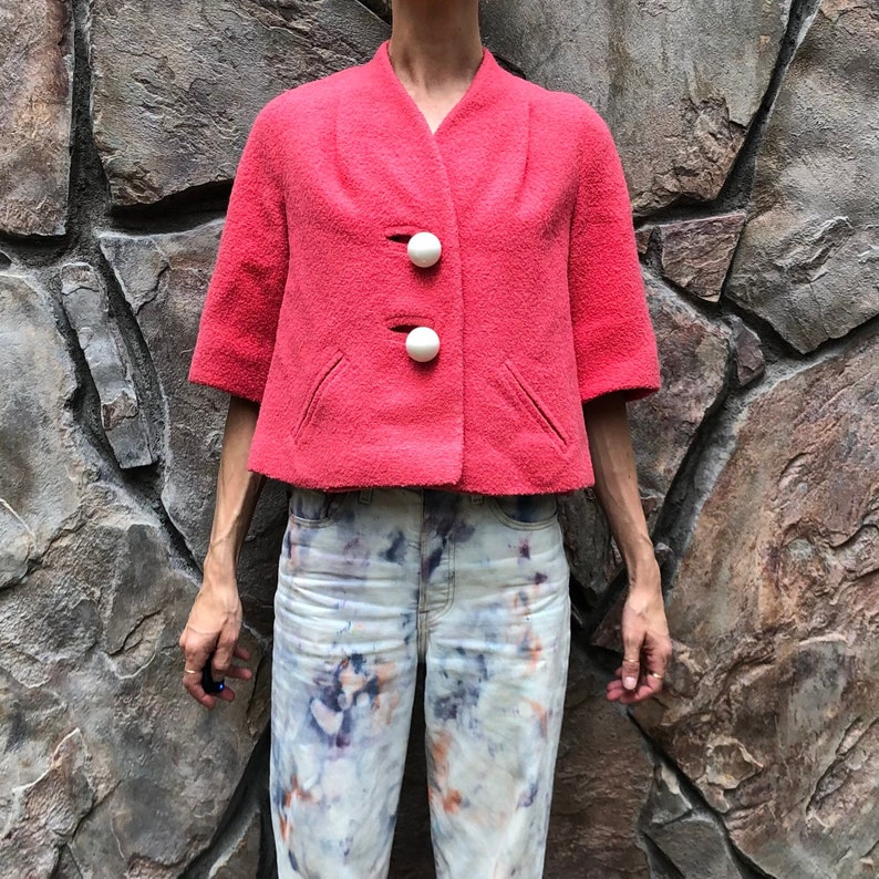May include: A pink cropped jacket with white buttons. The jacket is made of a soft, fuzzy material.