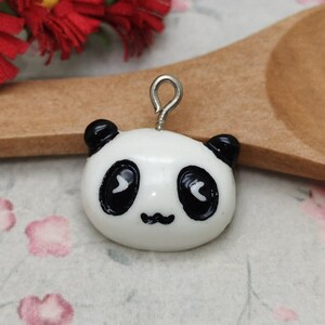 May include: A white panda charm with black eyes and a black nose. The charm has a silver loop for attaching to a necklace or bracelet.