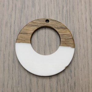 May include: A round wooden pendant with a white centre. The pendant has a hole at the top for hanging.