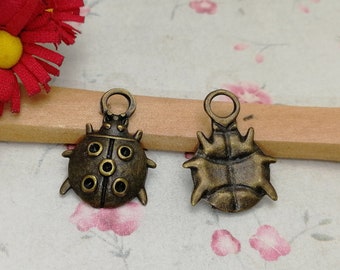 May include: Two antique bronze charms in the shape of ladybugs. One charm has a detailed design with spots and the other has a more abstract design.