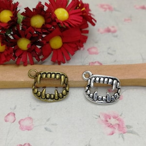 May include: Two silver charm pendants in the shape of a set of fangs. One pendant is antique gold and the other is silver.