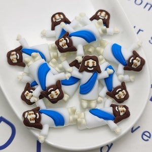 May include: A white plate filled with small, colorful, plastic figurines of Jesus. The figurines are all wearing white robes with blue sashes. They have brown hair and brown eyes.