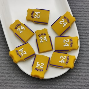 May include: Seven yellow and purple basketball jersey-shaped charms with the text "BRYANT 24" on each charm.