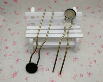 Puede incluir: Dos horquillas de bronce antiguo con una base redonda decorativa. Las horquillas tienen un diseño curvo y se muestran sobre un banco blanco contra un fondo floral. Estos accesorios para el cabello son adecuados para varios peinados.