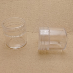 Puede incluir: Dos recipientes de plástico transparente con tapas. Los recipientes son cilíndricos y tienen un acabado liso y brillante.