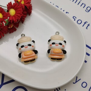 May include: Two white and black panda bear charms with orange aprons and white hats. The charms have silver jump rings.