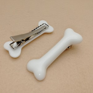 May include: Two white plastic bone-shaped hair clips. One clip has a silver metal spring.