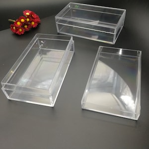 May include: Three clear plastic boxes of different sizes. The boxes are empty and have a rectangular shape.
