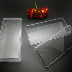 May include: Three clear plastic rectangular boxes with lids. The boxes are empty and are arranged on a black surface.