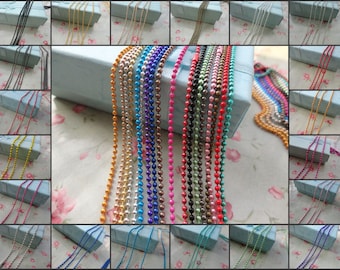 Può includere: Assortimento di 18 collane a catena metallica in vari colori, tra cui argento, oro, rosso, blu, verde e viola. Le catene sono esposte su uno sfondo blu con un motivo floreale bianco.