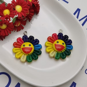 Puede incluir: Dos encantos de girasol de resina de color arcoíris con una cara sonriente. Los encantos tienen un lazo plateado para sujetar a un collar o pulsera.