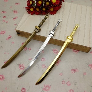 May include: Three decorative sword charms in gold, silver, and bronze finishes. The swords are detailed with intricate designs and have a loop at the top for attaching to a necklace or bracelet.
