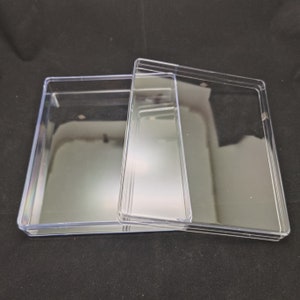 Op de afbeelding: Een transparante plastic doos met een deksel. De doos is leeg en heeft een rechthoekige vorm.