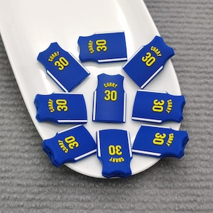 May include: Eight blue and white basketball jersey-shaped charms with the word "Curry" and the number "30" printed in yellow on each charm.