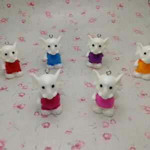 Pode incluir: Seis estatuetas de elefante brancas com camisas de diferentes cores. Os elefantes estão vestindo camisas vermelhas, azuis, roxas, laranja, rosa e rosa.