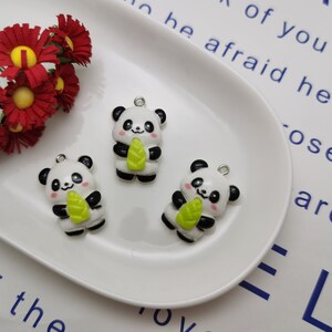May include: Three white and black panda bear charms with green bamboo leaves. The charms are on a white plate.