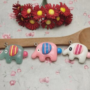 Peut inclure: Trois petits charmes en forme d'éléphant avec des corps de couleurs différentes et des motifs rayés. Les éléphants sont en pâte polymère et ont des anneaux de saut argentés pour la suspension.
