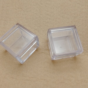 Może przedstawiać: Dwa kwadratowe pudełka z przezroczystego plastiku z pokrywkami. Pudełka są puste i wyglądają na wykonane z cienkiego, przezroczystego plastiku.