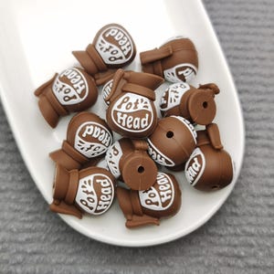 May include: A group of brown silicone charms shaped like a pot with the text "Pot's Head" on each charm.