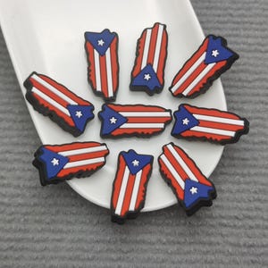 May include: A set of nine red, white, and blue Puerto Rican flag charms. The charms are shaped like the island of Puerto Rico and feature a white star in the center of the flag.