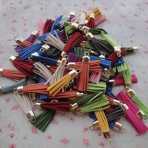 May include: A pile of colorful tassel keychains with gold metal rings. The tassels are made of various colors, including red, blue, green, yellow, and white.
