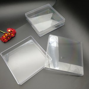 Puede incluir: Tres cajas cuadradas de plástico transparente con tapas. Las cajas están vacías y están sobre una superficie negra.