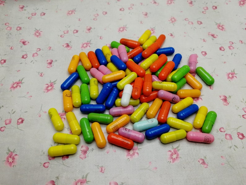 May include: A large pile of colorful capsules, mostly in shades of yellow, orange, green, blue, and pink. There is one white capsule in the center of the pile.