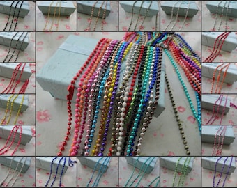 May include: Assortment of colorful metal chain necklaces with ball links. The chains are displayed on a light blue background with white floral pattern.