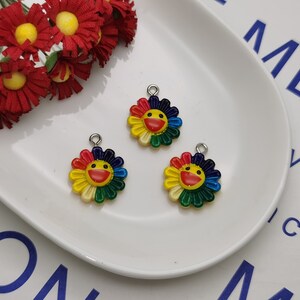 Puede incluir: Tres abalorios de flores coloridos con caras sonrientes. Cada abalorio está hecho de metal y tiene un bucle para sujetarlo a un collar, una pulsera o un llavero.
