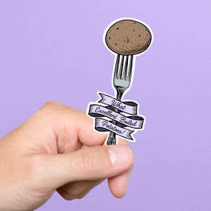 May include: A sticker featuring a brown potato impaled on a silver fork. A banner below the fork reads "What Excellent Boiled Potatoes!" in black script. The sticker is held against a purple background.