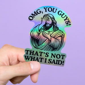 Może przedstawiać: Holograficzna naklejka z ilustracją Jezusa zasłaniającego oczy. Naklejka zawiera napisy "OMG, YOU GUYS!" i "THAT'S NOT WHAT I SAID!" w czarnym tekście. Tło jest fioletowe.
