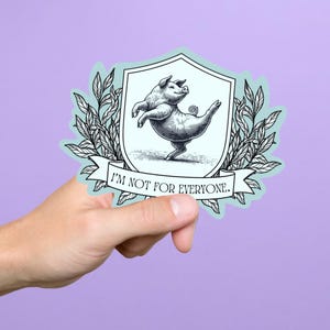 May include: A sticker featuring a whimsical illustration of a pig balancing on one foot within a shield-shaped emblem. The pig is depicted in a vintage style, with the text "I'M NOT FOR EVERYONE" on a banner below.