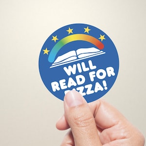 Puede incluir: Una pegatina redonda azul con el texto "WILL READ FOR PIZZA!". Presenta un arco iris sobre un libro abierto y estrellas amarillas. La pegatina está sujeta por una mano sobre un fondo neutro.