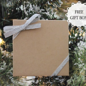 May include: A brown gift box with a silver ribbon tied in a bow. The box is sitting on a green Christmas tree.