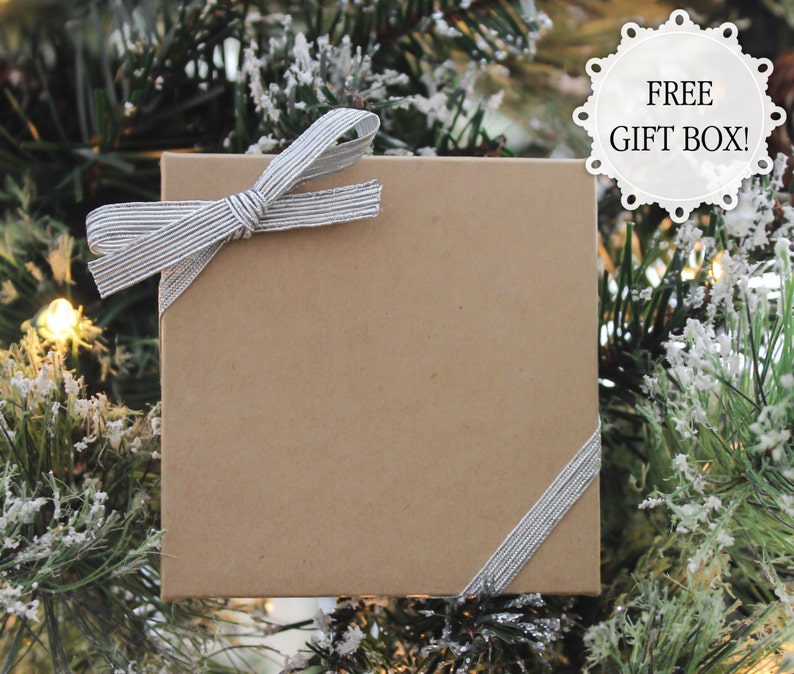 May include: A brown gift box with a silver ribbon tied in a bow. The box is sitting on a green Christmas tree.