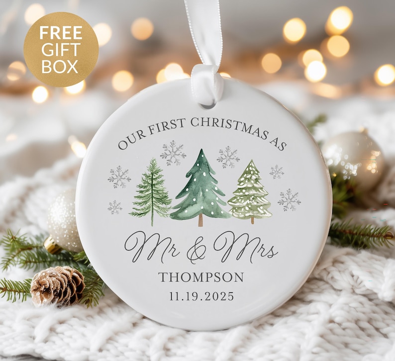 May include: White ceramic Christmas ornament with a ribbon for hanging. The ornament features watercolor illustrations of pine trees and snowflakes, with the text "OUR FIRST CHRISTMAS AS Mr & Mrs Thompson 11.19.2025".