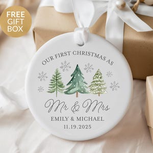 May include: A white ceramic Christmas ornament with the text "OUR FIRST CHRISTMAS AS Mr & Mrs" and the names "EMILY & MICHAEL" with the date "11.19.2025". The ornament features watercolor-style Christmas trees and snowflakes.
