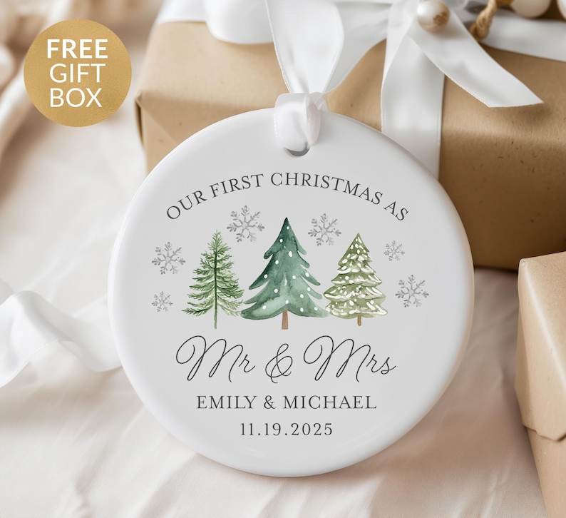 May include: A white ceramic Christmas ornament with the text "OUR FIRST CHRISTMAS AS Mr & Mrs" and the names "EMILY & MICHAEL" with the date "11.19.2025". The ornament features watercolor-style Christmas trees and snowflakes.