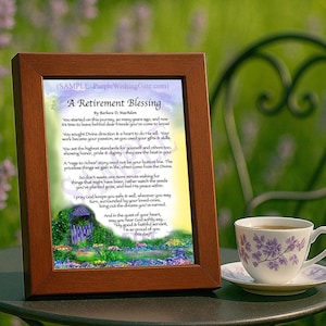 May include: A framed retirement blessing print with a brown wooden frame. The print features a poem with a colorful garden scene at the bottom. A teacup with a floral design sits on a saucer next to the frame.