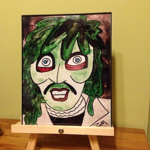 May include: A hand-painted portrait of a person with green hair, red eyes, and a wide smile. The portrait is framed and displayed on a wooden easel.