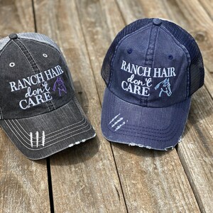 May include: Two trucker hats with the text "Ranch Hair don't care" and a horse silhouette embroidered on the front. One hat is black with a gray mesh back, the other is blue with a black mesh back.